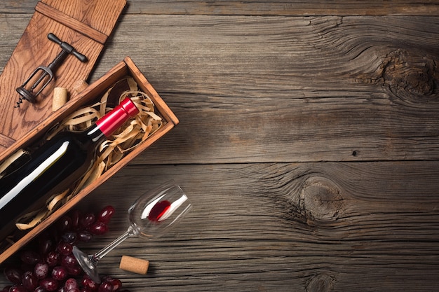 Vin rouge dans une boîte avec un verre et un tire-bouchon sur une table en bois. Vue de dessus avec un espace pour vos salutations