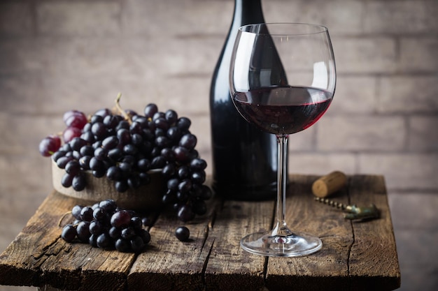 Vin rouge dans un verre et raisins mûrs sur table en bois