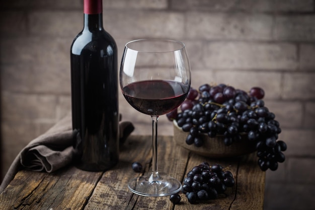 Vin rouge dans un verre et raisins mûrs sur table en bois