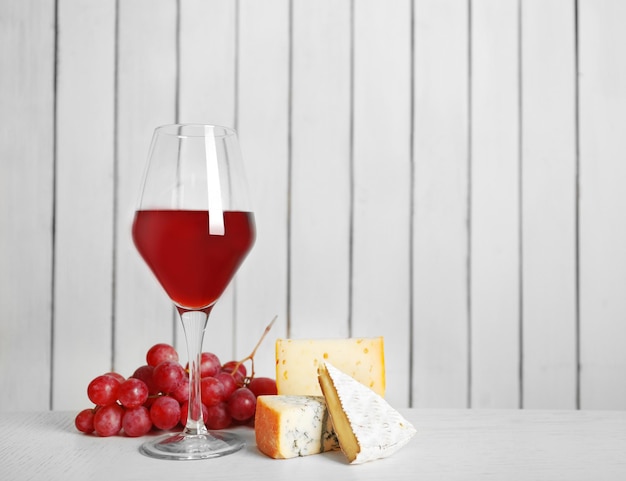 Vin rouge avec du fromage et du raisin sur fond de mur en bois