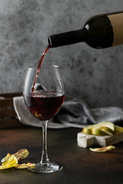 Le vin rouge est versé dans un verre sur un fond gris foncé Il y a des poires sur le plateau sur la table