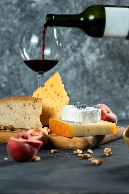 Vin rouge et fromage. Différents types de fromage avec noix, lavande et pêche aux figues sur une planche à découper. Dîner romantique. Copiez l'espace pour la conception. Fond sombre. Flou artistique. verser le vin dans un verre