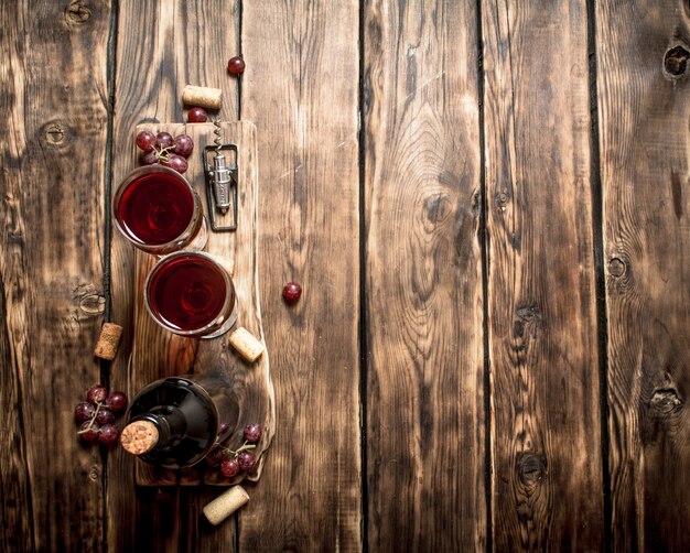 Vin rouge sur planche de bois avec des bouchons et un tire-bouchon. Sur une table en bois.