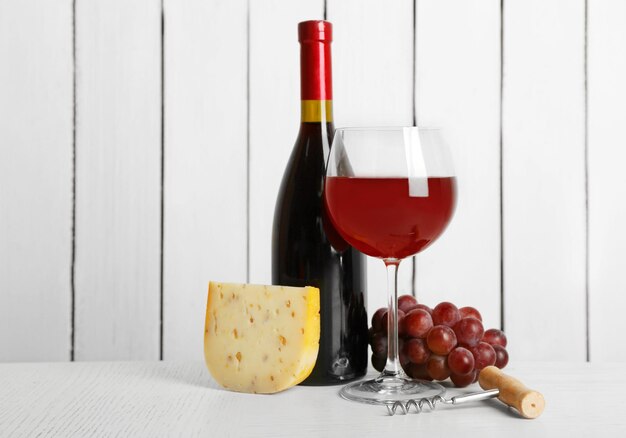 Vin rouge avec raisin et fromage sur fond de mur en bois