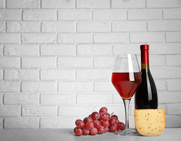 Vin rouge avec raisin et fromage sur fond de mur de briques