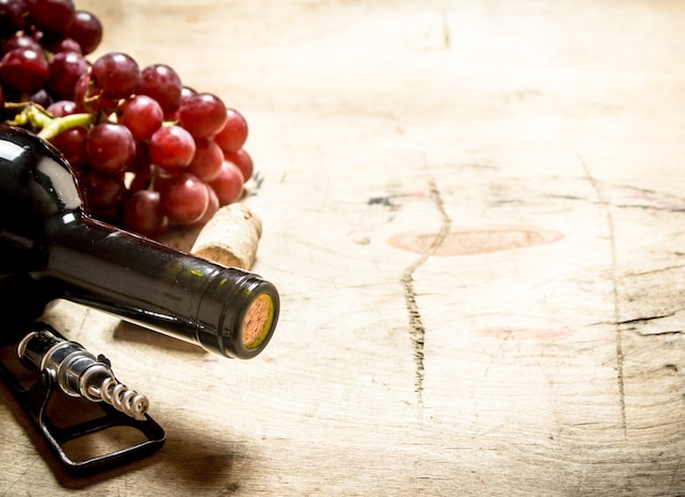 Vin rouge avec un tire-bouchon, des raisins et des bouchons sur fond de bois