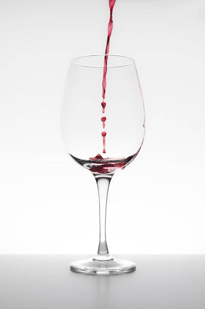 Photo vin rouge tombant dans le verre sur fond blanc