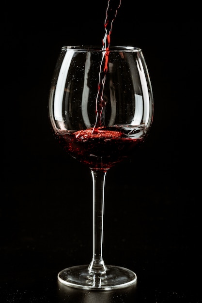 Vin rouge versé dans un verre à vin sur un fond sombre