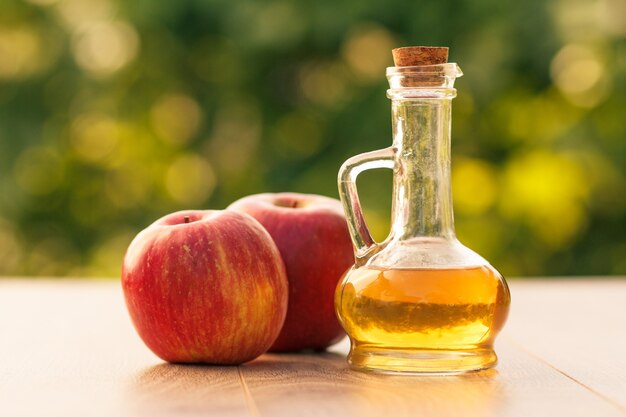 Vinaigre de cidre de pomme dans une bouteille en verre avec du liège et des pommes rouges fraîches sur des planches de bois avec fond naturel vert flou. faible profondeur de champ. Aliments biologiques pour la santé