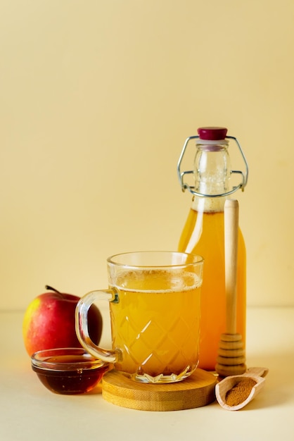 Vinaigre de cidre de pomme dans une tasse en verre et une bouteille avec du miel et des pommes rouges à la cannelle sur fond jaune