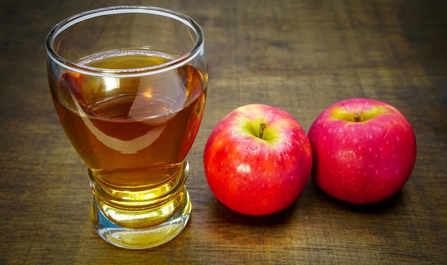 vinaigre de cidre de pomme dans un verre avec des pommes sur le plancher en bois