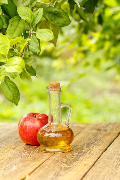 Vinaigre de pomme dans une bouteille en verre avec du liège et pomme rouge fraîche sur de vieilles planches de bois avec fond naturel vert flou. Aliments biologiques pour la santé