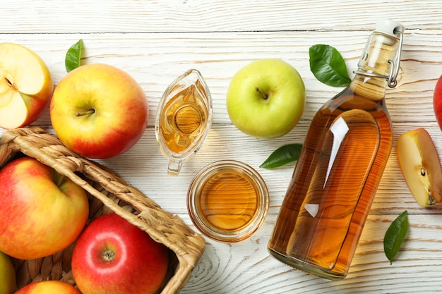 Vinaigre de pomme fait maison et ingrédients sur table en bois blanc