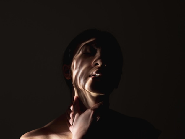 Violence féminine Violence domestique Pression sociale Portrait d'art de la silhouette de femme victime souffrante avec les mains sur la gorge motif abstrait d'ombre sur le visage isolé sur fond d'espace de copie de nuit noire