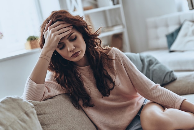 Virus de la grippe. Jeunes femmes malades souffrant de maux de tête alors qu'elles étaient assises sur le canapé à la maison