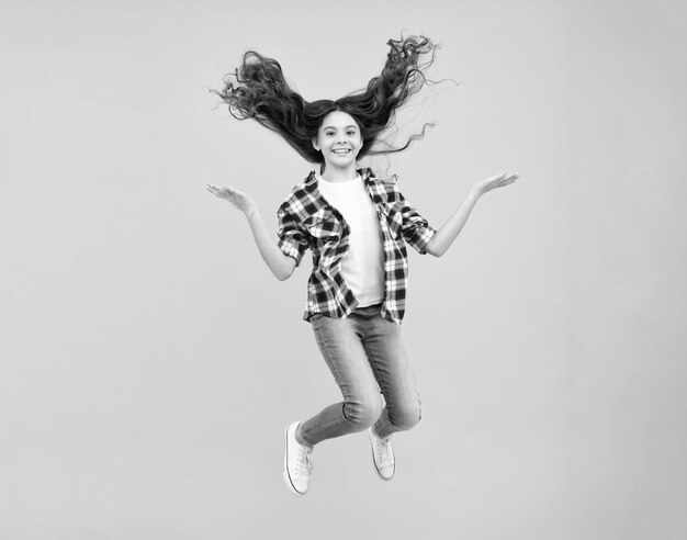 Un visage d'adolescente avec des cheveux de mouvement fou, du bonheur, de la liberté de mouvement et d'un enfant, une jeune adolescente sautant en l'air sur un fond jaune.