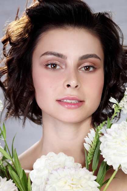 Visage de beautéBelle femme avec un maquillage naturel léger et une peau parfaite avec des fleurs