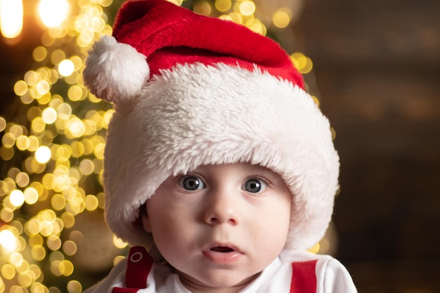 Visage de bébé mignon en bonnet de noel près de l'arbre de noël enfance heureuse enfant année nouvel an enfants