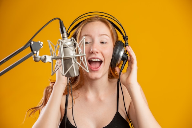 Visage de belle femme rousse chantant avec un microphone à condensateur argent bouche ouverte effectuant la chanson pose sur l'espace de copie de mur jaune pour votre texte Annonceur radio FM.