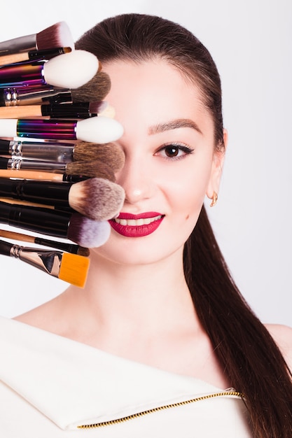 Le visage d'une belle fille et pinceau de maquillage sur mur blanc