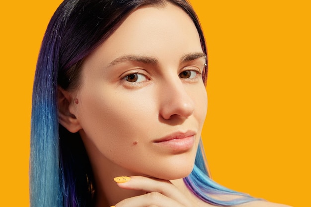 Visage de belle jeune femme aux cheveux bleus sur fond jaune Concept de traitement de salon de beauté
