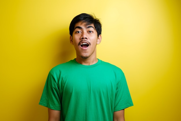 Visage choqué d'un homme asiatique en t-shirt vert sur fond jaune