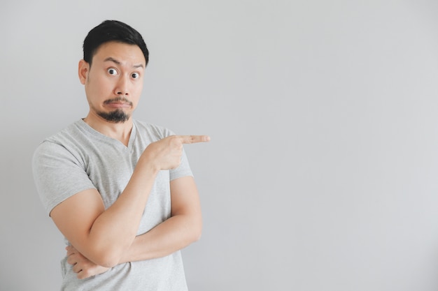 Visage choqué de l&#39;homme en t-shirt gris avec la main pointent sur un espace vide.