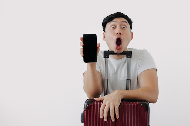Le visage choqué et surpris d'un homme utilisant une application de téléphone portable pour voyager assis avec ses bagages ou