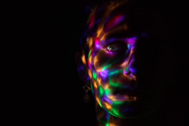 un visage dans l'obscurité recouvert de taches de couleur vive provenant d'une lampe brillante éblouissement de couleur provenant de la lampe