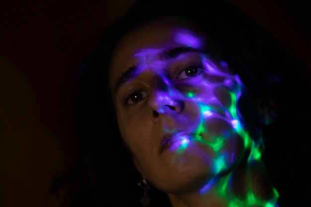 un visage dans l'obscurité recouvert de taches de couleur vive provenant d'une lampe brillante éblouissement de couleur provenant de la lampe