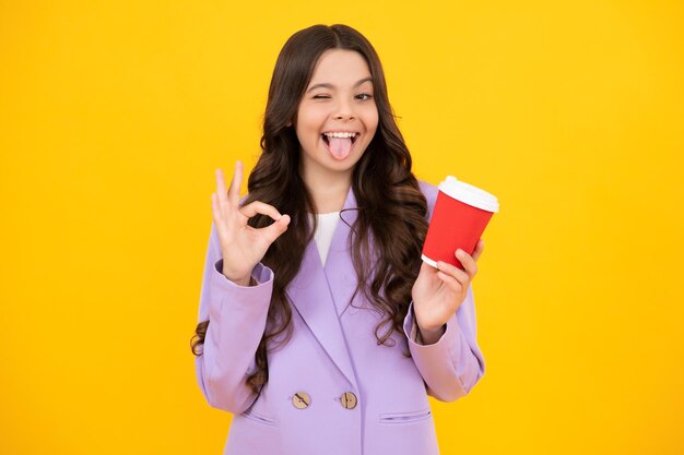 Photo visage drôle adolescent fille tenant une tasse de café ou de thé chaud enfant avec une tasse à emporter sur jaune