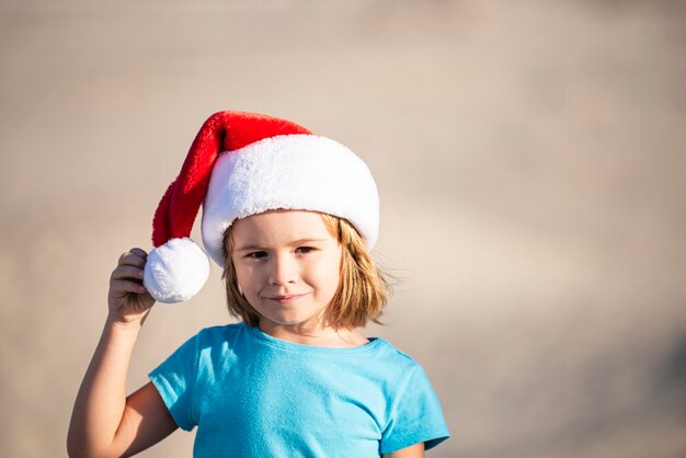 Visage drôle de mignon petit garçon en bonnet de noel près de la plage le jour ensoleillé portrait d'enfant de noël