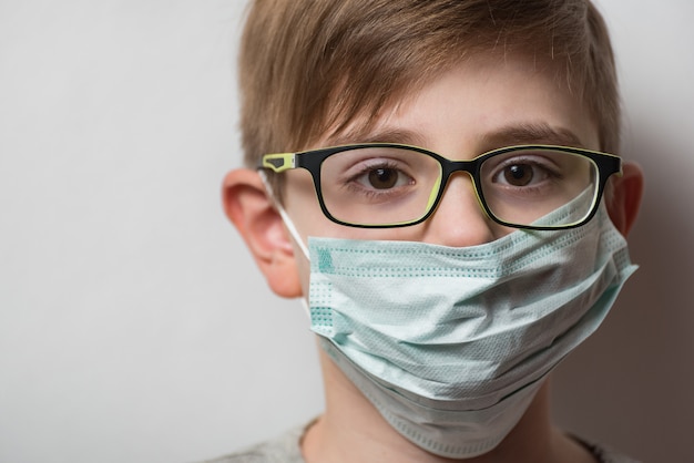 Visage de l'enfant avec des lunettes et un masque de protection jetable. Garçon portant un masque de protection contre la grippe