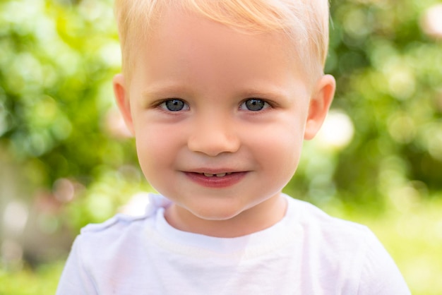 Visage d'enfant de sourire agrandi. Cortrait de garçon enfant souriant sur fond extérieur.