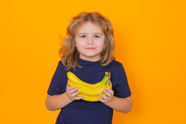 Visage d'enfants avec des fruits Enfant tenir la banane en studio Portrait en studio d'un garçon mignon avec des bananes isolé sur fond jaune espace de copie