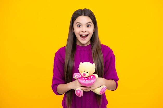 Visage excité Adolescente dans des vêtements décontractés tenir peluche pour anniversaire sur fond jaune Enfant passer du temps avec ses jouets Expression étonnée joyeuse et heureuse