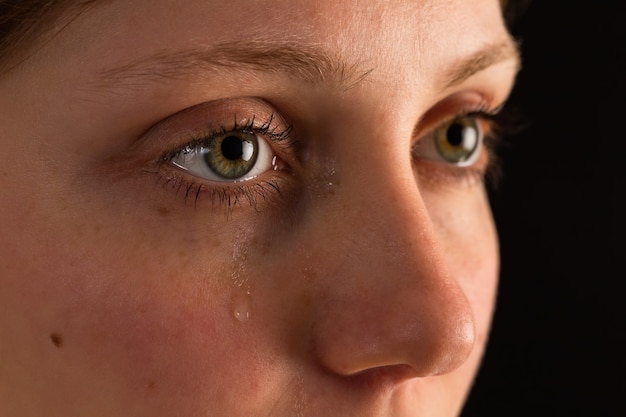 Visage de femme malheureuse en larmes de gros plan dans l'obscurité.