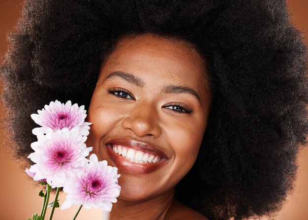 Visage de femme noire ou cheveux afro avec des fleurs de marguerite sur fond de studio pour un soin doux de la peau, une lueur vibrante ou une dermatologie biologique Zoom portrait ou modèle de beauté sourire heureux avec des cheveux naturels et des plantes