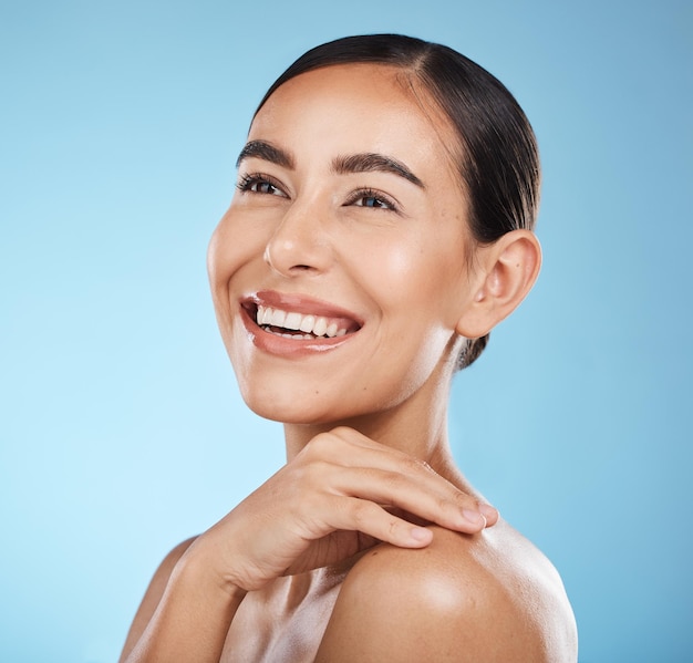 Visage de femme et sourire heureux et beauté avec des cosmétiques naturels et lueur isolée sur fond bleu Nettoyer les soins cosmétiques et la main avec le maquillage du visage et une peau saine avec des soins de la peau en studio