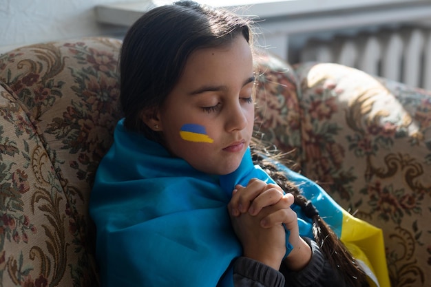 Le visage d'une fille effrayée un enfant pleurant des larmes coulant peintes sur sa joue dans les couleurs jaune bleu du drapeau ukrainien une demande d'aide Les enfants demandent la paix