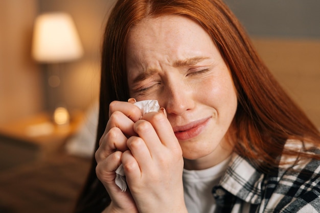 Visage en gros plan d'une jeune femme triste pleurant et essuyant des larmes avec un mouchoir souffrant d'une mauvaise relation se sentant seule assise seule sur le lit à la maison
