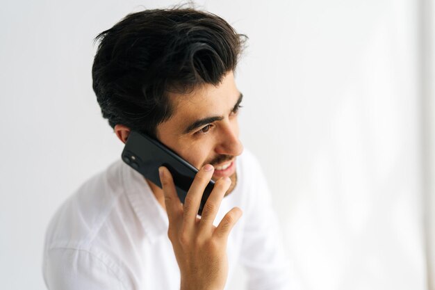 Visage en gros plan d'un jeune homme d'affaires barbu joyeux parlant de téléphone portable ayant une conversation sur un smartphone tenant et utilisant un téléphone portable