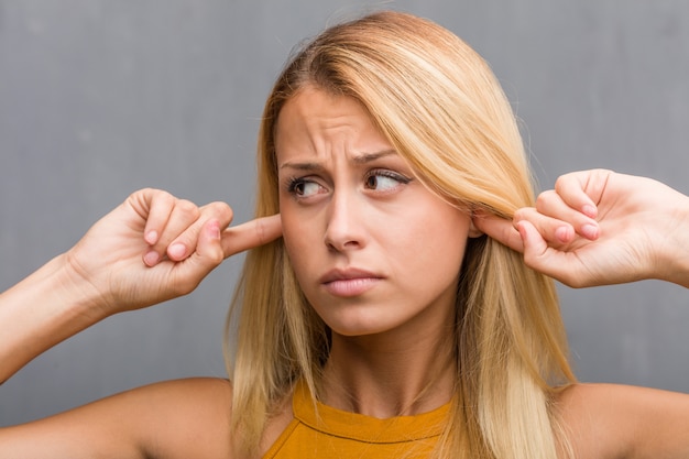 Photo visage gros plan, portrait d'une jeune femme blonde naturelle couvrant les oreilles avec les mains, en colère et fatiguée d'entendre du son