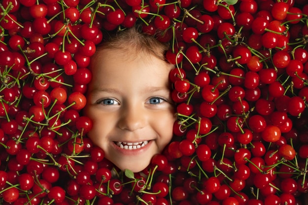 Visage d'un heureux entouré d'un gros tas de fruits de cerises juteuses mûres rouges