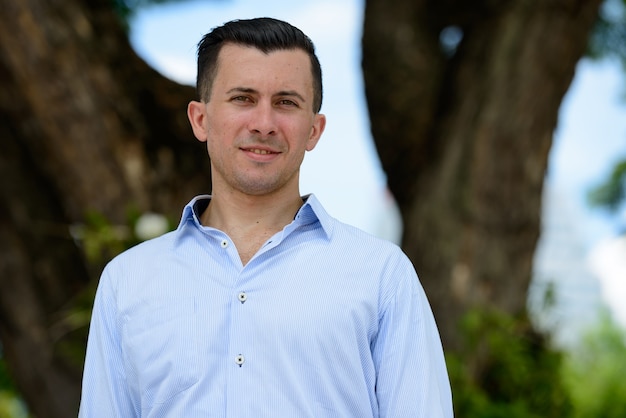 Visage d'heureux jeune bel homme d'affaires souriant dans le parc