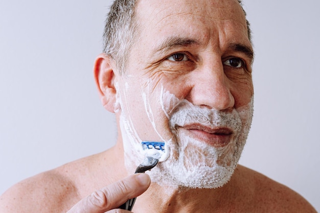 visage d'un homme d'âge moyen en gros plan, yeux bruns, avec du chaume sur le visage, recouvert de mousse à raser