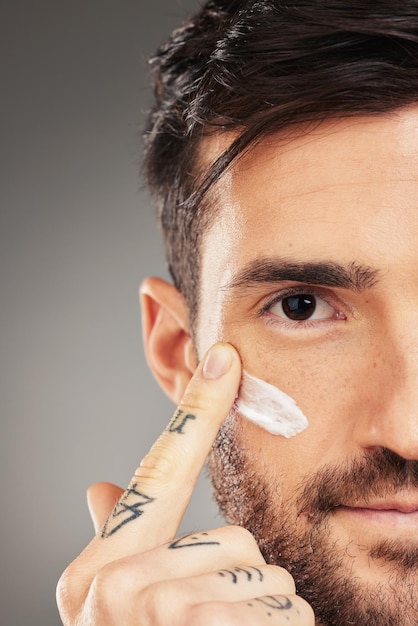 Visage d'homme et crème pour les soins de beauté et le bien-être avec la main sur un fond de studio gris avec maquette Modèle masculin avec lotion pour le visage sur lotion solaire pour la santé de la peau et la protection contre les uv