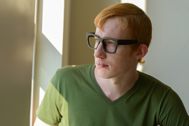 Visage d'homme nerd aux cheveux rouges regardant par la fenêtre