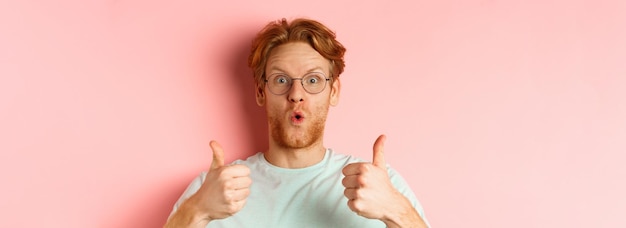 Photo visage d'un homme rousse heureux dans des verres et un t-shirt montrant le pouce levé et l'air excité d'approuver et de pra