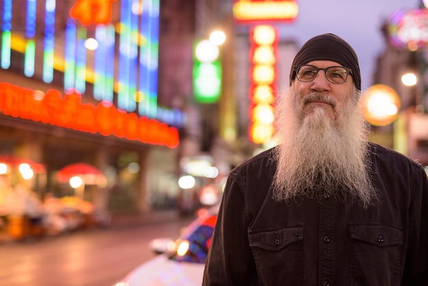 Visage de l'homme touriste barbu mature avec des lunettes pensant dans Chinatown la nuit